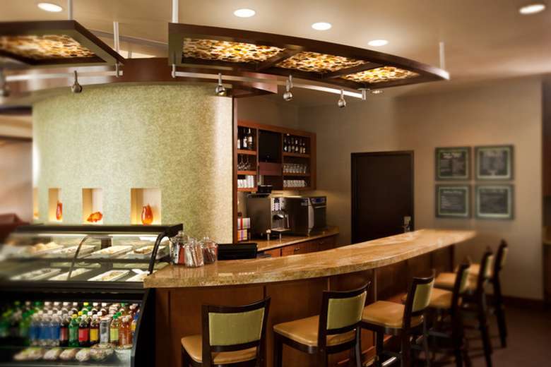 wood bar with several stools in front and a variety of fruit drinks, coffee dispensers, wines and other alcoholic beverages