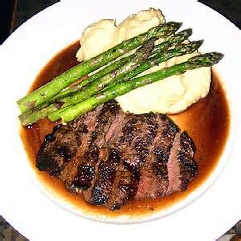 sliced steak on a plate with asparagus, mashed potatoes, and sauce