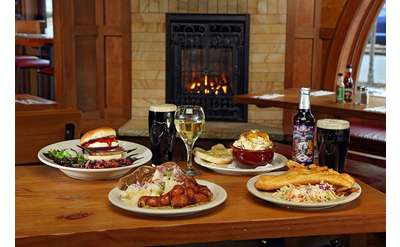 plates of food and drinks on a wooden table in a restaurant, a fireplace in the background