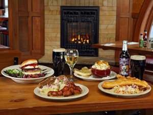 plates of food and drinks on a wooden table in a restaurant, a fireplace in the background