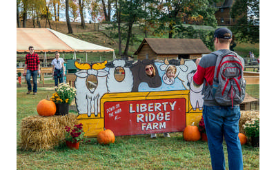 man taking photo of people with heads in cut out image of farm animals