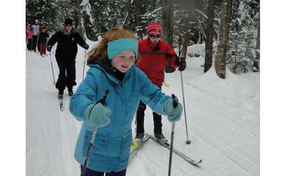 three people cross-country skiing with a young girl dressed in blue in the lead