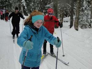 three people cross-country skiing with a young girl dressed in blue in the lead