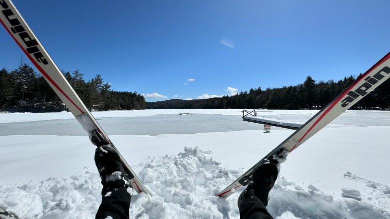 person lying down in snow with skis looking out at lake