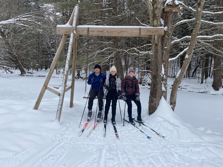 three friends in skis sit on bench