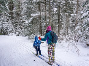 mom and kid cross-country skiing into the woods