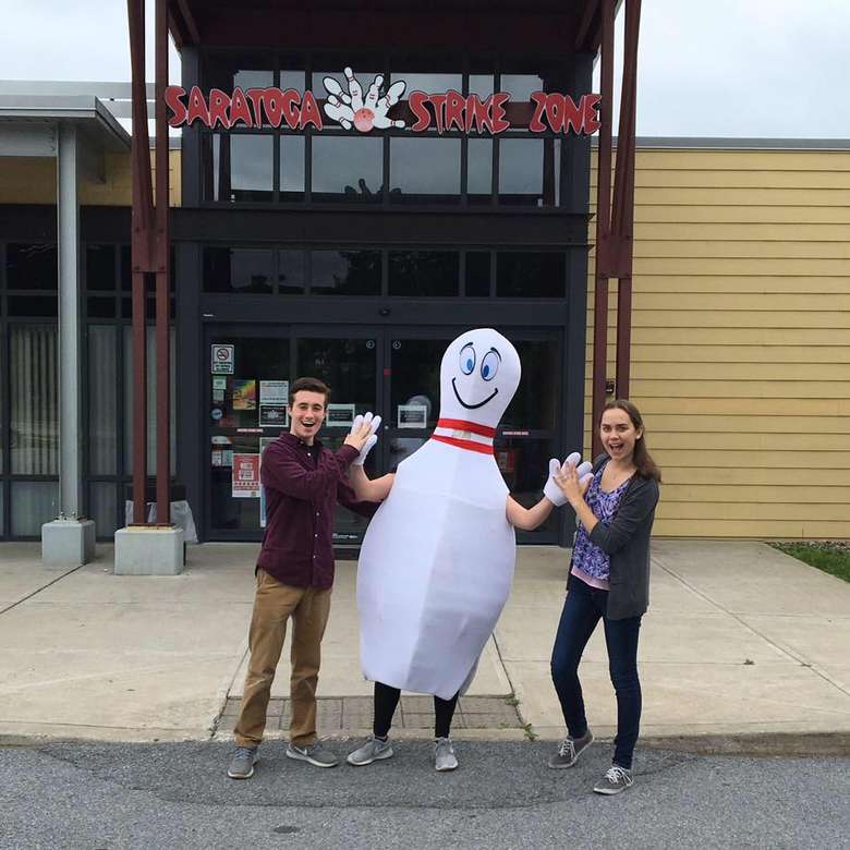 a man and woman standing with someone dressed as a bowling pin