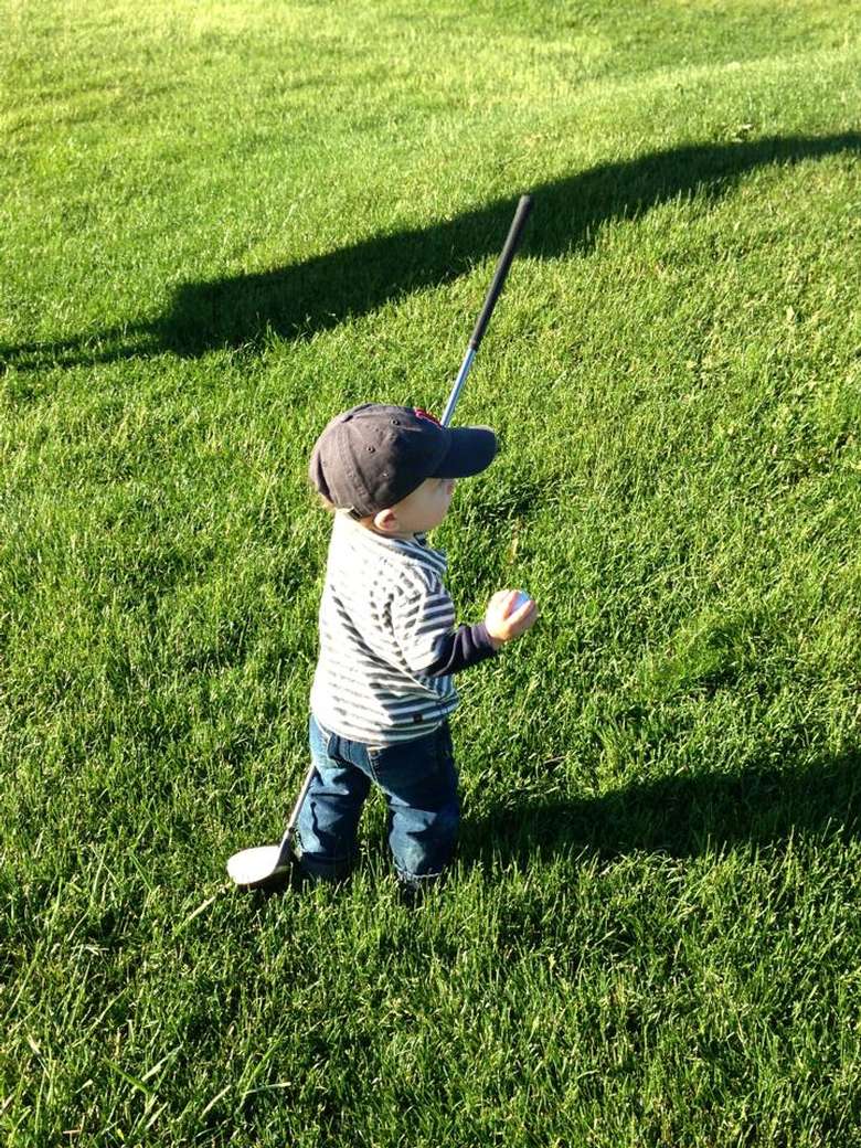 A little boy with a golf club and ball standing in the grass