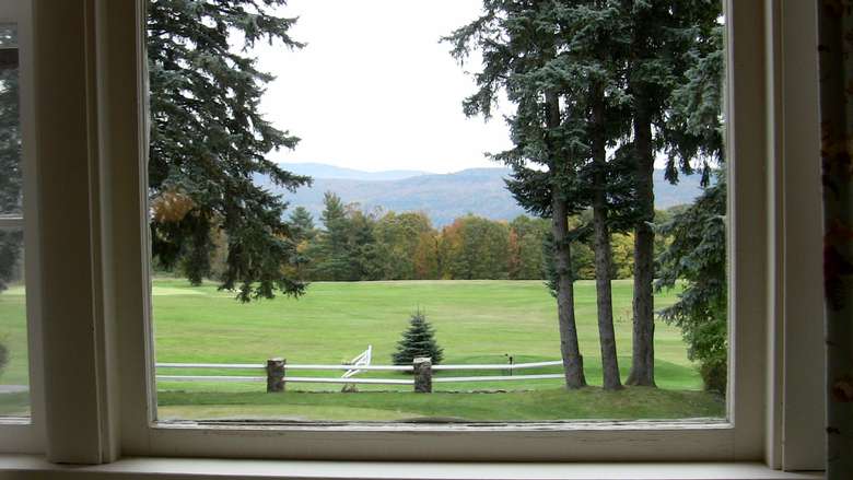 view out of a window onto a big field with trees and mountains behind it
