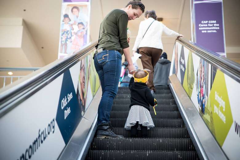 a woman helping a toddler up an escalator