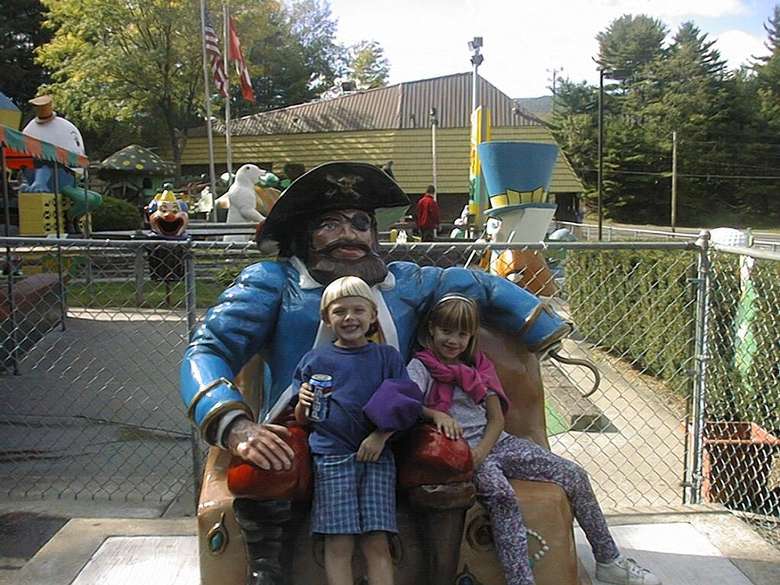 A young boy and a young girl sitting on a bench with a pirate statue