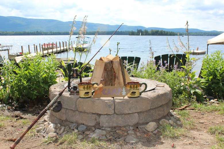 a fire pit with Adirondack-style mugs on it, water in the background