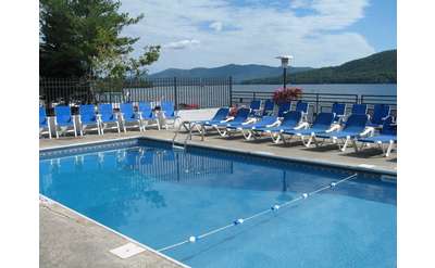 blue lounge chairs surrounding a pool overlooking lake george