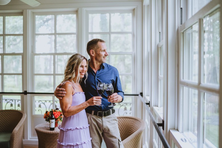 a man and woman standing side by side with wine glasses in a hotel room