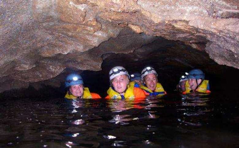four people in life jackets and helmets floating in water inside of a cave
