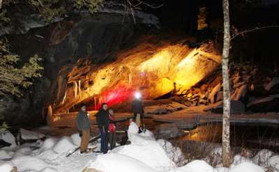 four people snowshoeing in front of a lit cave entrance