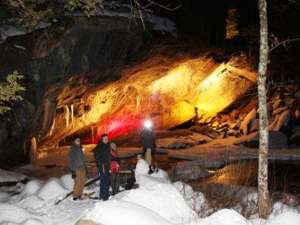 four people snowshoeing in front of a lit cave entrance