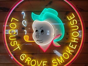 Neon sign for Locust Grove SmokeHouse featuring a pig with a cowboy hat and a pipe.