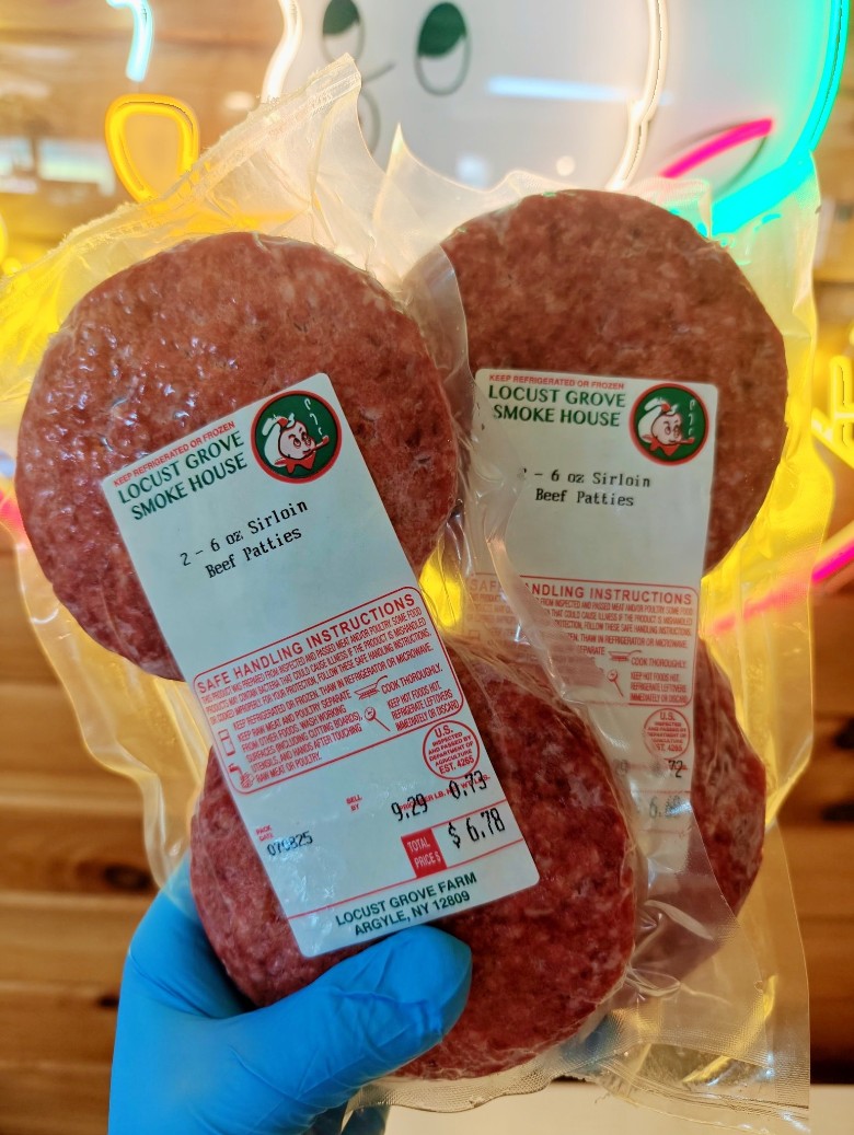 Two packages of Locust Grove SmokeHouse Sirloin Beef Patties held in a gloved hand.