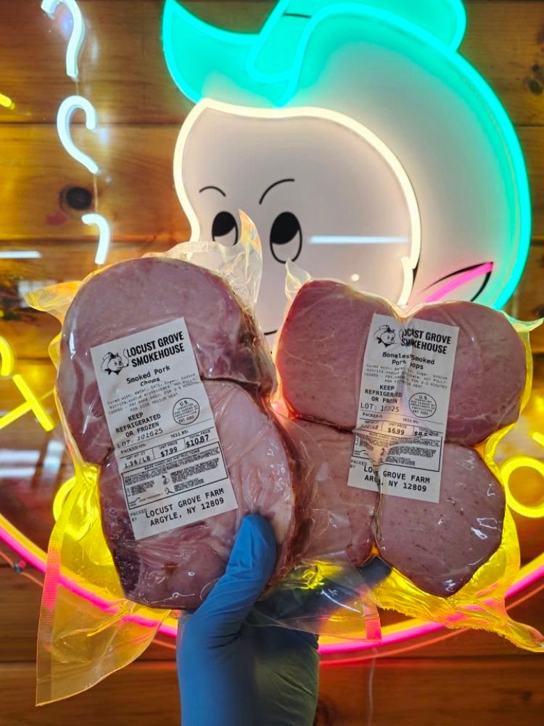 Packaged Smoked Pork Chops held in front of the Locust Grove Smokehouse neon sign.