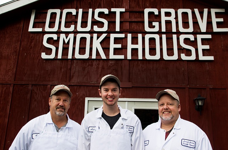 Three men in white aprons standing outside the Locust Grove Smokehouse building.