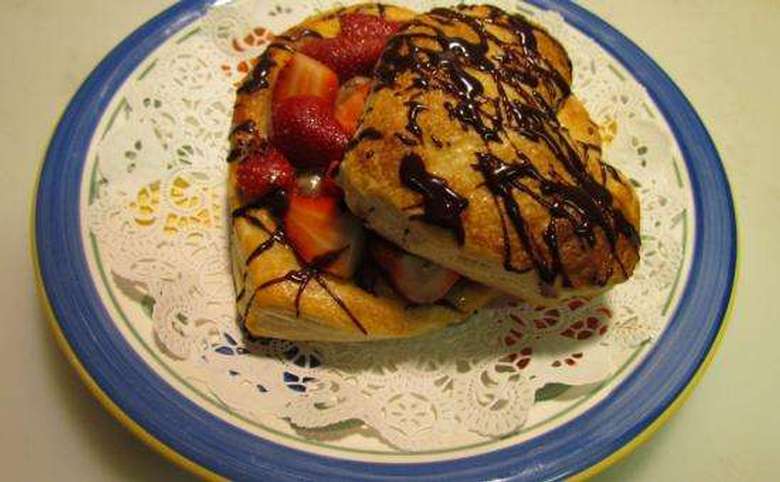two heart-shaped pastries with a chocolate drizzle and strawberries on top