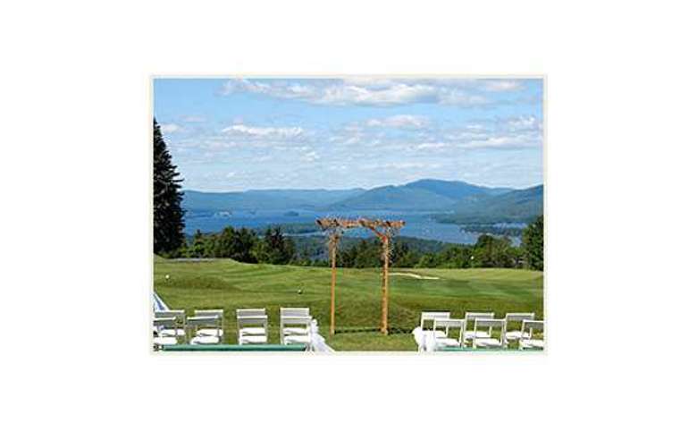 a green lawn set with white chairs and a wooden trellis for an outdoor wedding ceremony with the forest, lake and mountains in the background