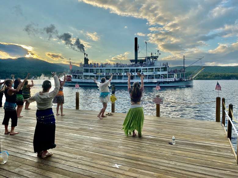 women dancing on boat dock with steamboat traveling by