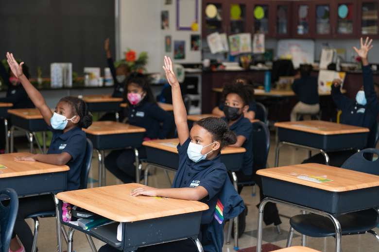 a few young students raising their hand in a classroom