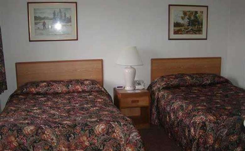 A motel room with two beds, a nightstand with lamp, phone and clock in-between the beds, and one picture over each bed. The bedspreads are a burgundy floral multi-color.