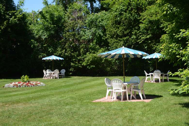 three plastic tables, each with four chairs and a striped umbrella, spread out in different parts of a large green lawn