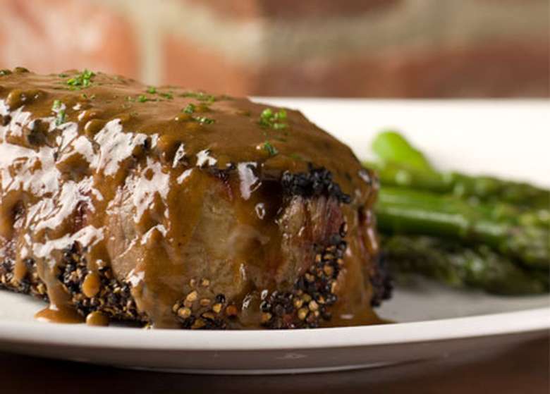 steak with a pepper cream sauce on a white plate with asparagus