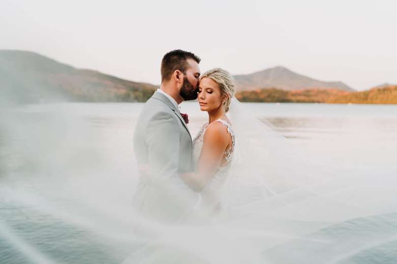 bride and groom embrace in front of fall scene with water
