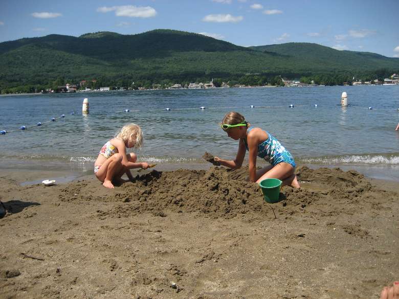 Two girls playing in the sand at Usher's Park Beach with lake george and mountains in the background
