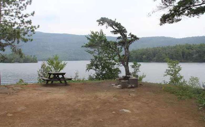 a fairly clear campsite with a picnic table with the lake in the background