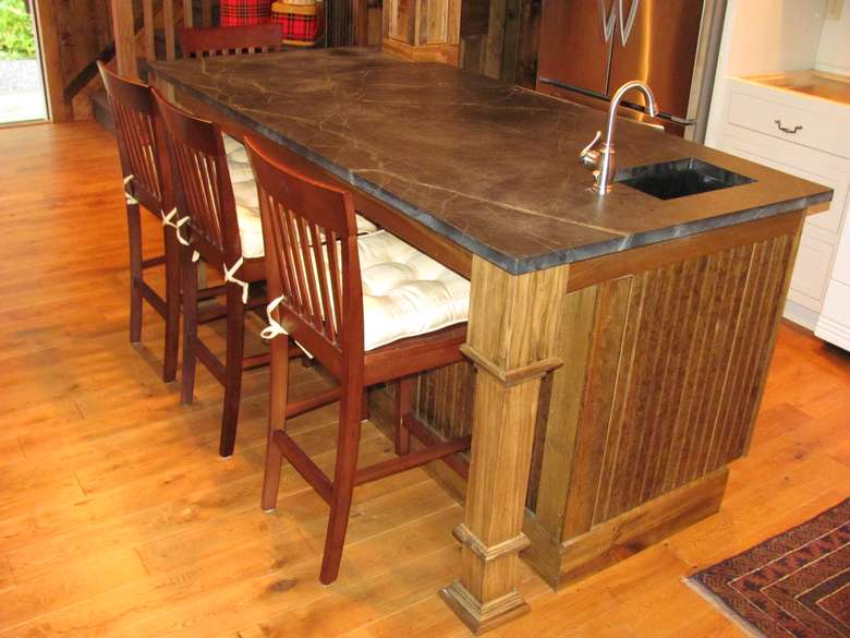 a wooden and rustic looking kitchen island with chairs around it