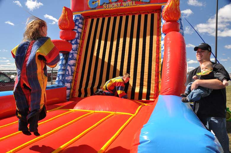 Kids jumping on an inflated sticky Velcro wall while their dad looks on