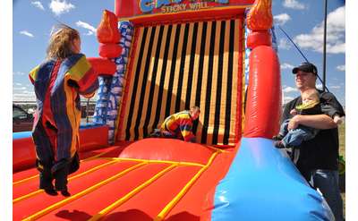 Kids jumping on an inflated sticky Velcro wall while their dad looks on