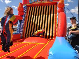Kids jumping on an inflated sticky Velcro wall while their dad looks on