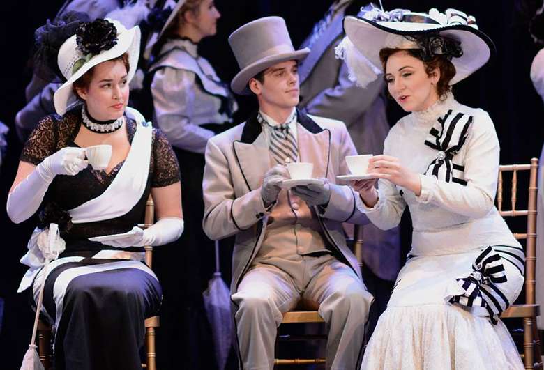 three people on stage in Victorian clothing having tea