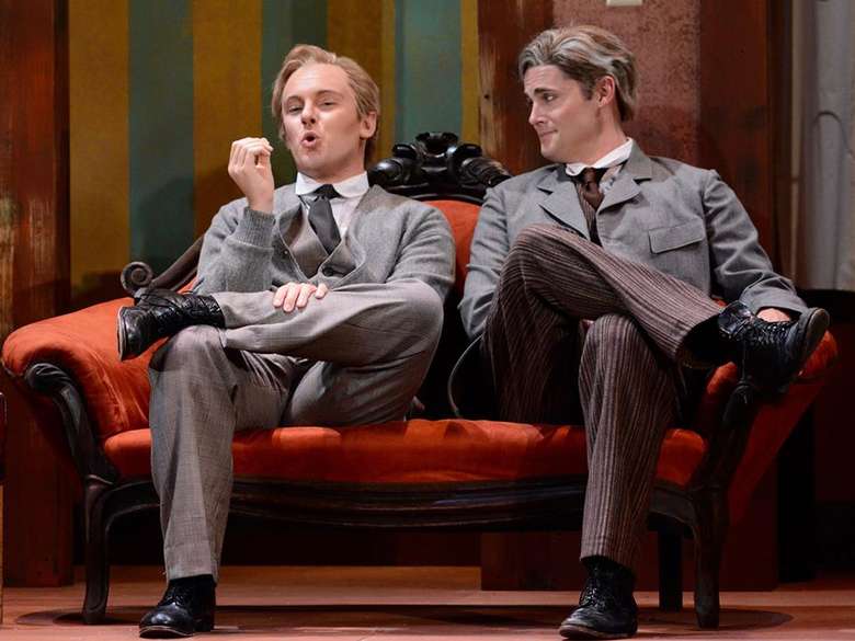 two men in suits on stage sitting on a couch