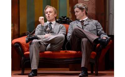 two men in suits on stage sitting on a couch