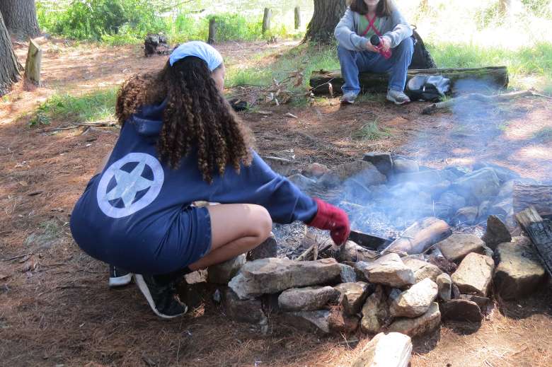 a teenager makes food using a frying pan over a campfire