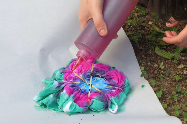 a rolled up t-shirt is having dye squirted on it from a squeeze bottle