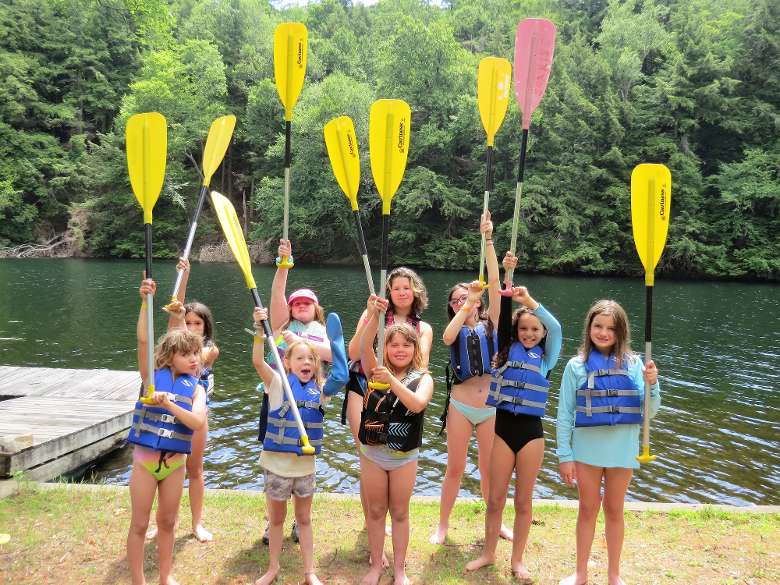 group of campers hold canoe paddles in the air
