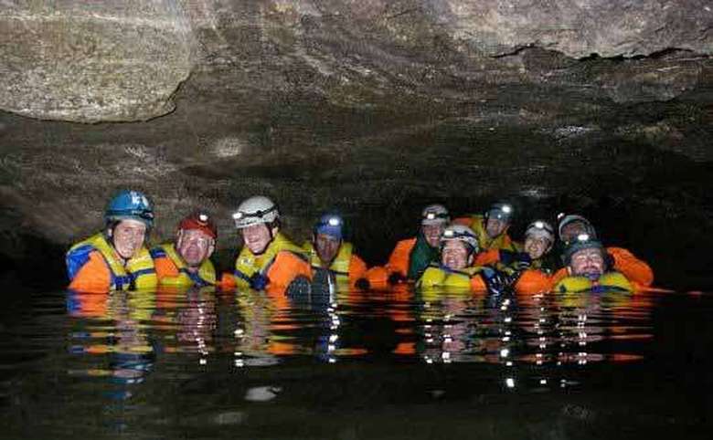 group of explorers in helmets and life jackets in a body of water in a cave