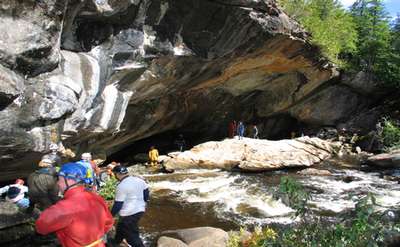 Group of visitors under a large overhang of rocks by a river