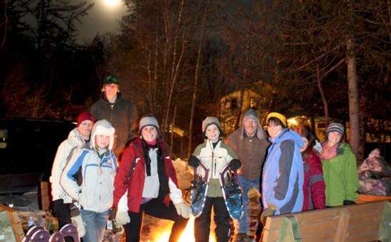 Group of people standing by fire, one is holding snowshoes