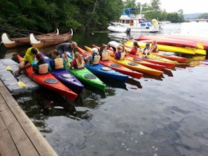 people in a rainbow of kayaks getting instruction before launching