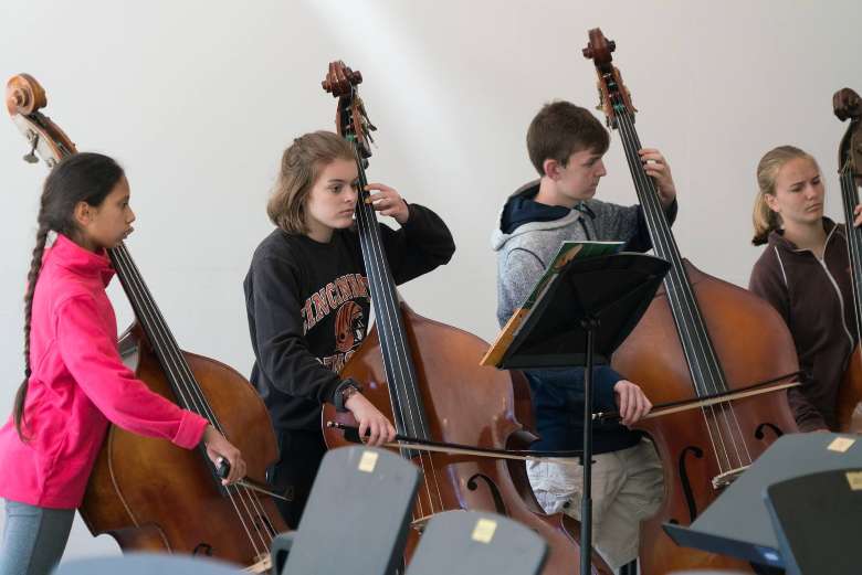 four young people playing cellos